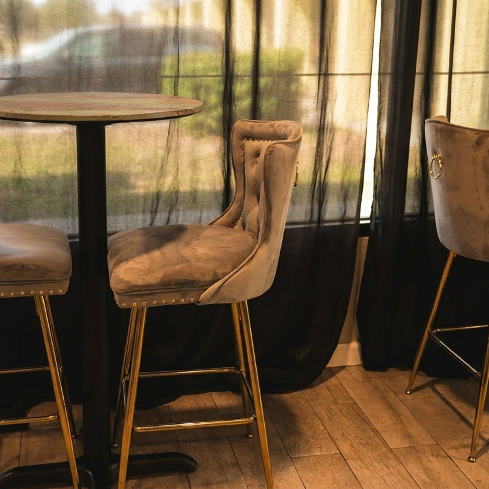 Three elegant velvet bar stools with gold legs surround two tall, round tables in a dimly lit room.
